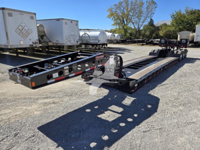 Trailer chassis showing hydraulic flip flatbed with multiple axles and tool compartments, metal frame, and wiring harness visible.