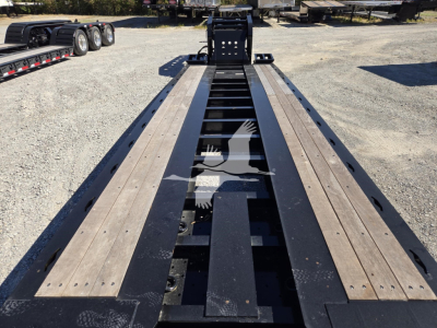 Trailer bed of a Fontaine lowboy with long wooden deck beams and hydraulic flip mechanism visible, center frame and landing gear, outdoor lot.