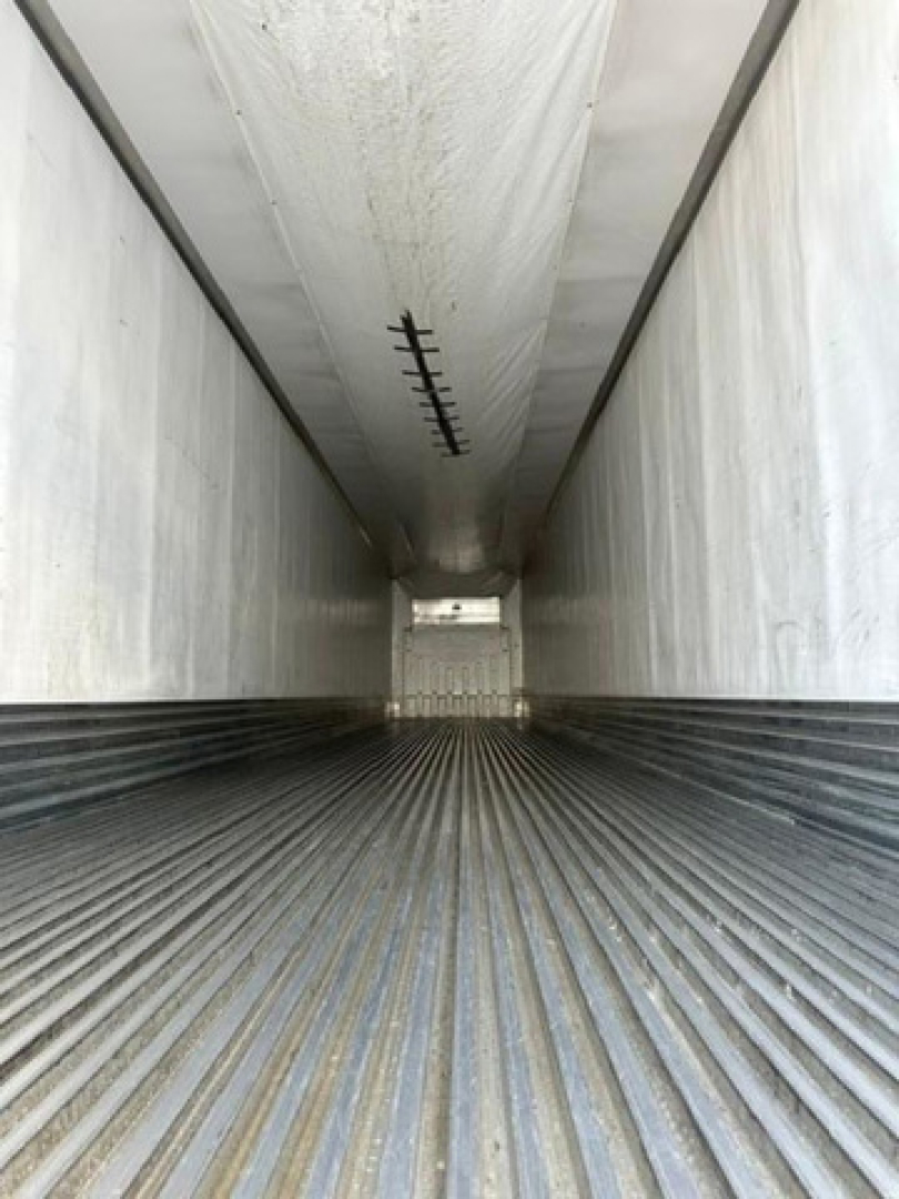 Trailer interior view of a refrigerated utility trailer cargo hold with ribbed floor and white walls, showing a rear doorway opening at far end.