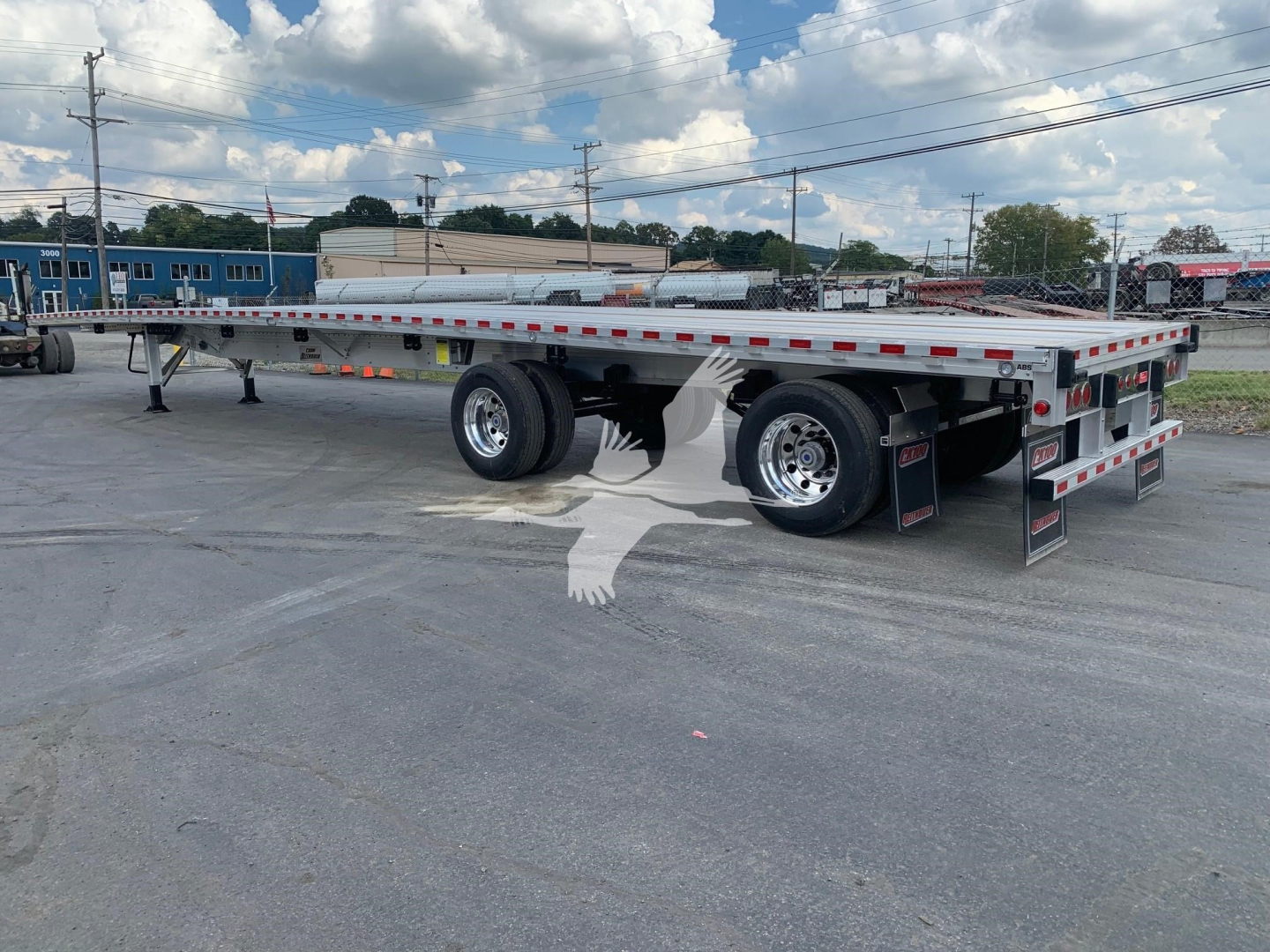 Flatbed trailer showing tandem axle with aluminum deck, side rails, rear ramps, and Reflective tape. Sticker labels and structural components visible.