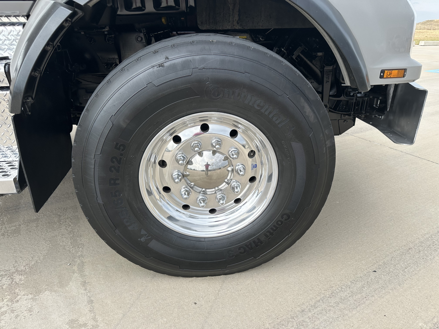 Kenworth T880 front wheel area showing large Continental truck tire and polished steel hub with multiple lug nuts; partial fender and step box visible.