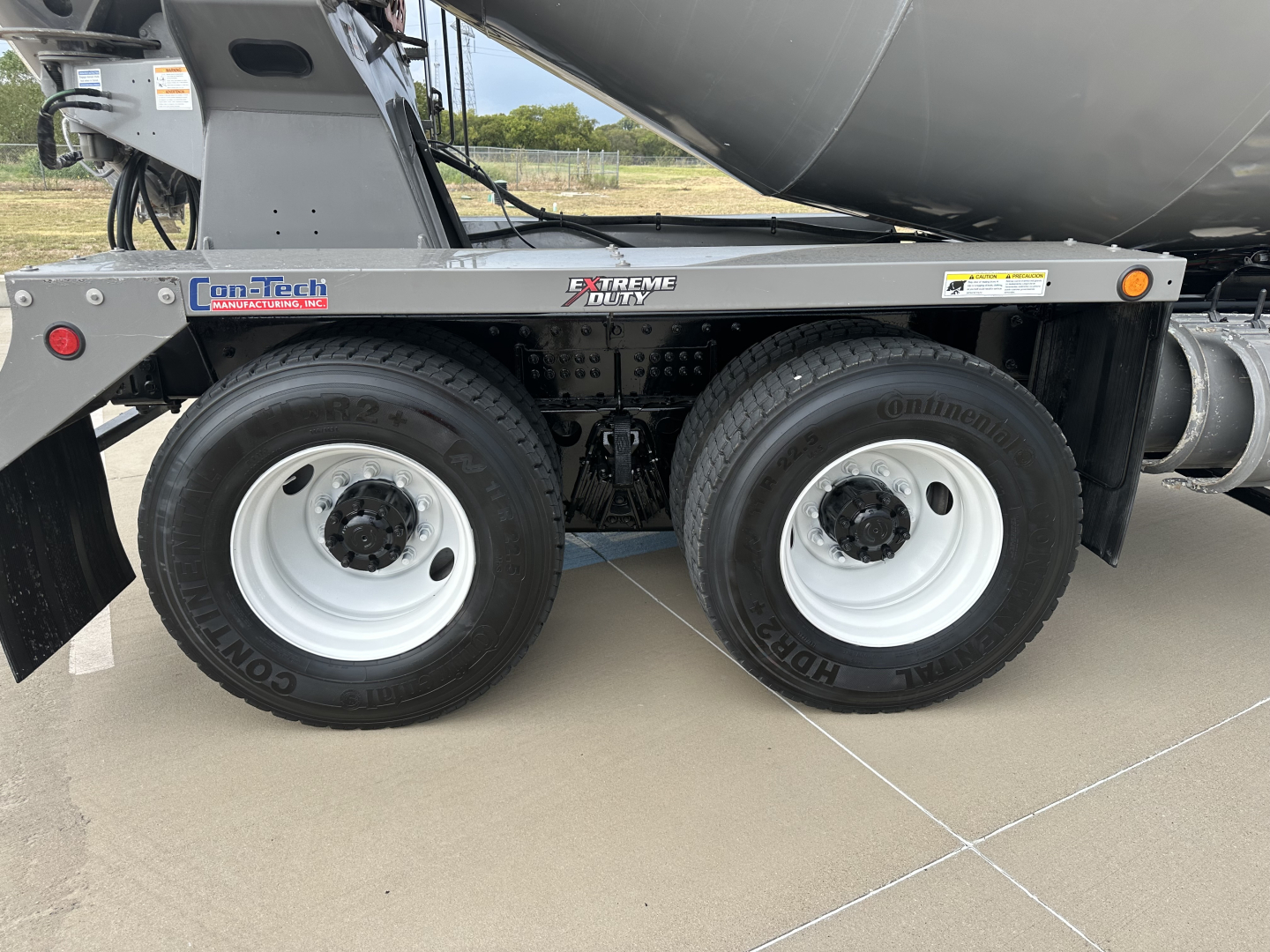Twin rear wheels of a mixer truck with white rims and heavy-duty tires; label decals on the frame reading Con-Tech, Xtreme Duty, and other small safety stickers visible.