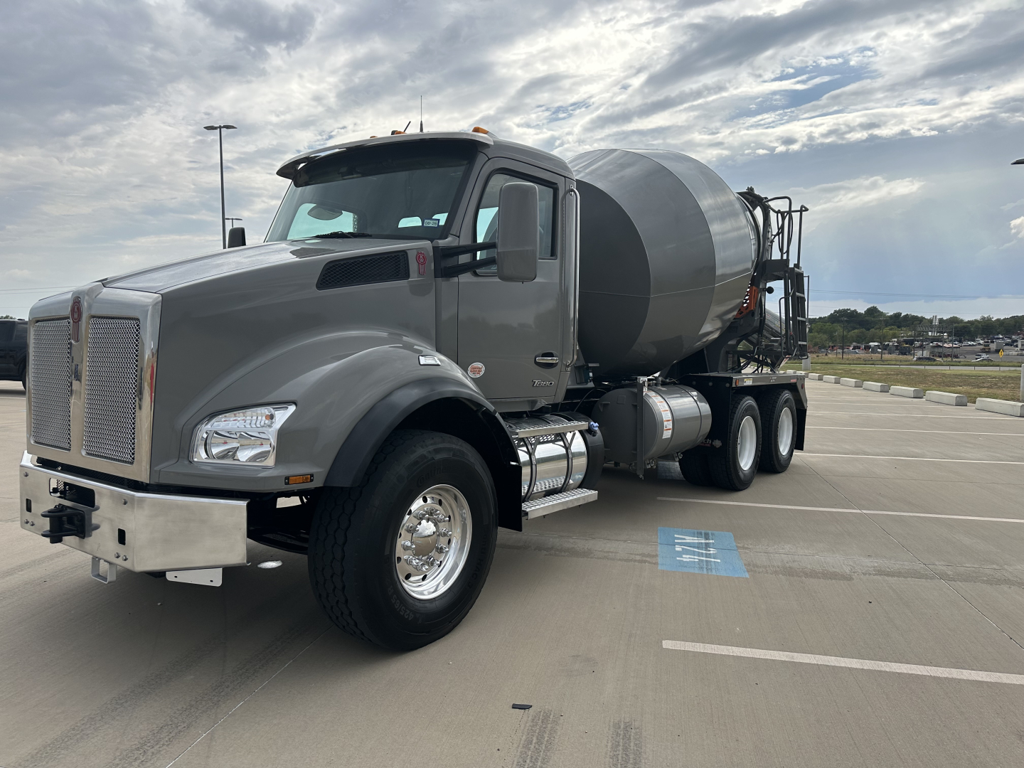 Kenworth T880 mixer truck in a parking lot, gray cab, cement mixer behind, front grille with chrome bumper, side mirrors, and fuel tanks visible.