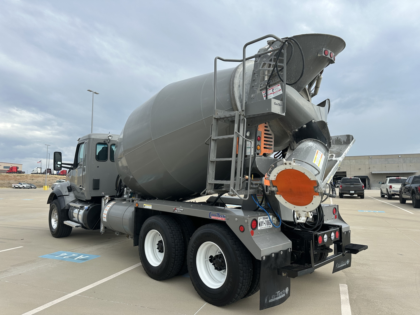 Mixer truck rear view showing concrete mixer batcher and chute, Kenworth T880 chassis, three axles, exhaust stack, and rear mudflaps.