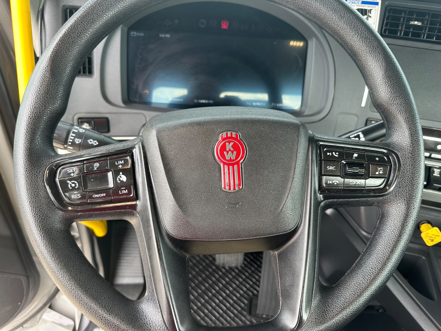 Steering wheel of a 2026 Kenworth T880 with KW logo, left and right control stalks visible showing buttons and dashboard screen behind.