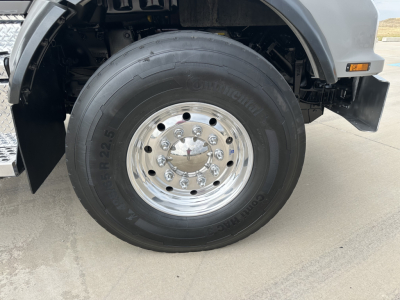 Kenworth T880 front wheel area showing large Continental truck tire and polished steel hub with multiple lug nuts; partial fender and step box visible.