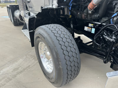 Kenworth T880 front wheel area showing heavy-duty tire and suspension components, partial engine bay and piping visible.