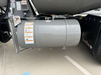 Kenworth T880 fuel tank underside showing cylindrical aluminum tank with safety stickers and mounting brackets.