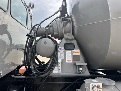 Kenworth mixer truck attachment with hydraulic hoses and hoses reel, mounted to rear of cab and fuel tank. Visible labels and safety stickers on mount.