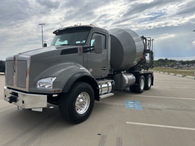 Kenworth T880 mixer truck in a parking lot, gray cab, cement mixer behind, front grille with chrome bumper, side mirrors, and fuel tanks visible.