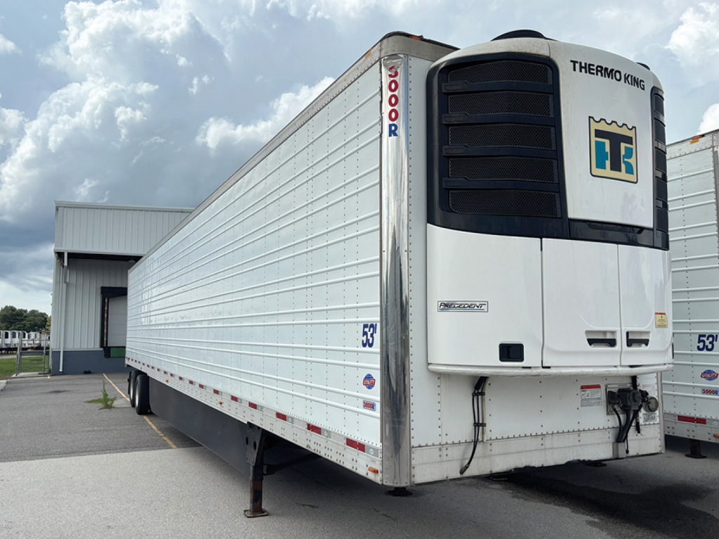 Utility 3000R trailer with Thermo King reefer unit at front, side view shows white corrugated metal body, multiple axles, and support legs; visible stickers and model numbers.