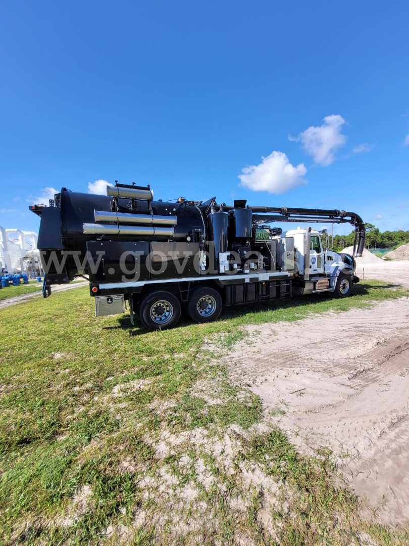 Truck-mounted vacuum system on a Mack GU713 chassis showing large vacuum unit and hoses.