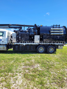 Mack GU713 vacuum truck side view showing large cylindrical tank with multiple hoses and compartments.