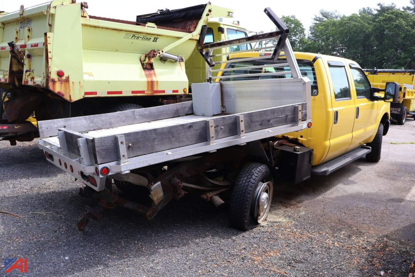 Ford F-350 Super Duty stake truck with a flatbed/utility bed and yellow cab, visible stake sides and metal toolbox, rear chassis and exposed frame.