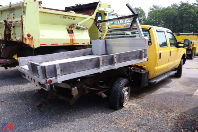 Ford F-350 Super Duty stake truck with a flatbed/utility bed and yellow cab, visible stake sides and metal toolbox, rear chassis and exposed frame.