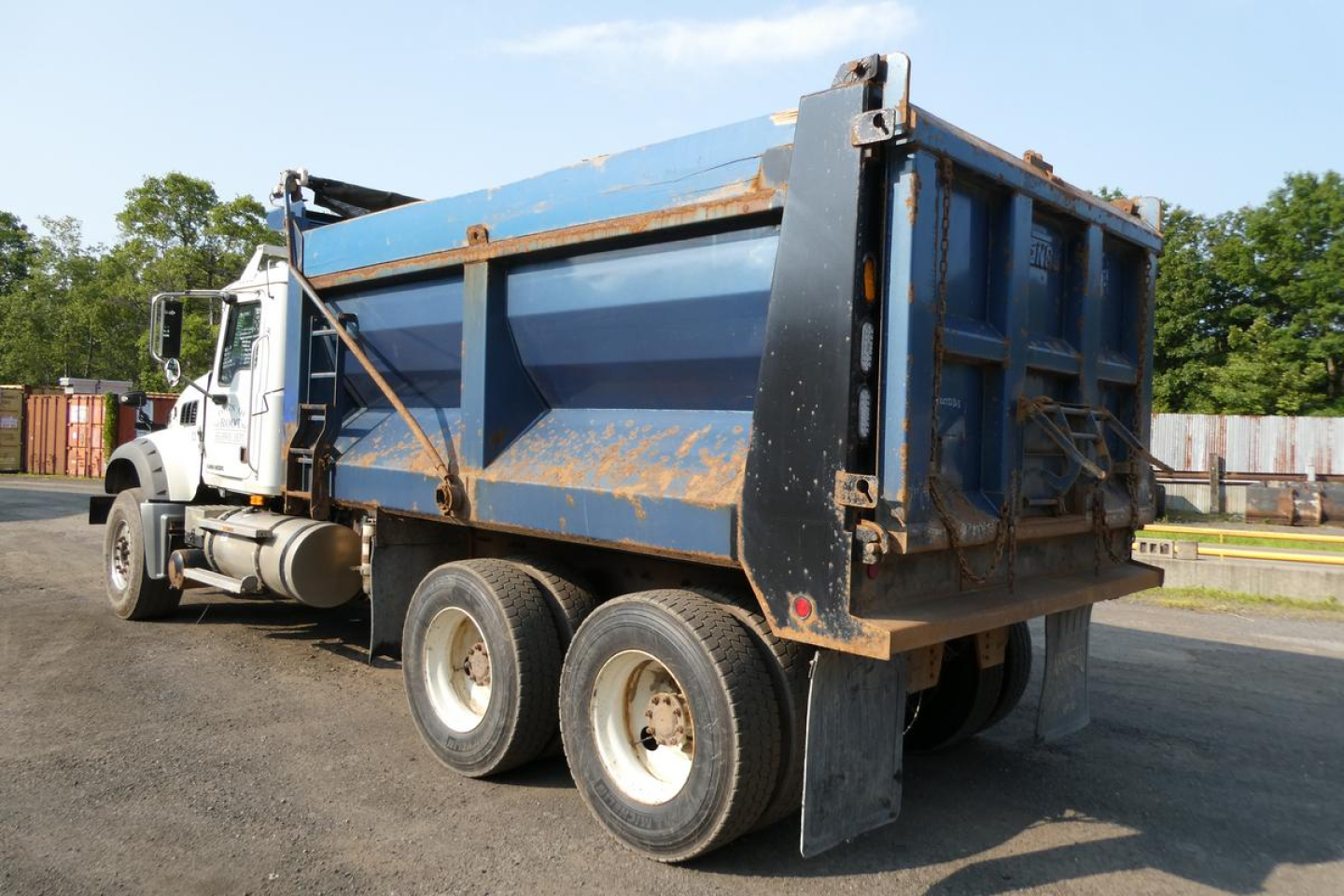 Dump truck rear and side view showing blue dump bed with black tailgate and white cab; six-wheel tandem rear with visible rust-prone edges.