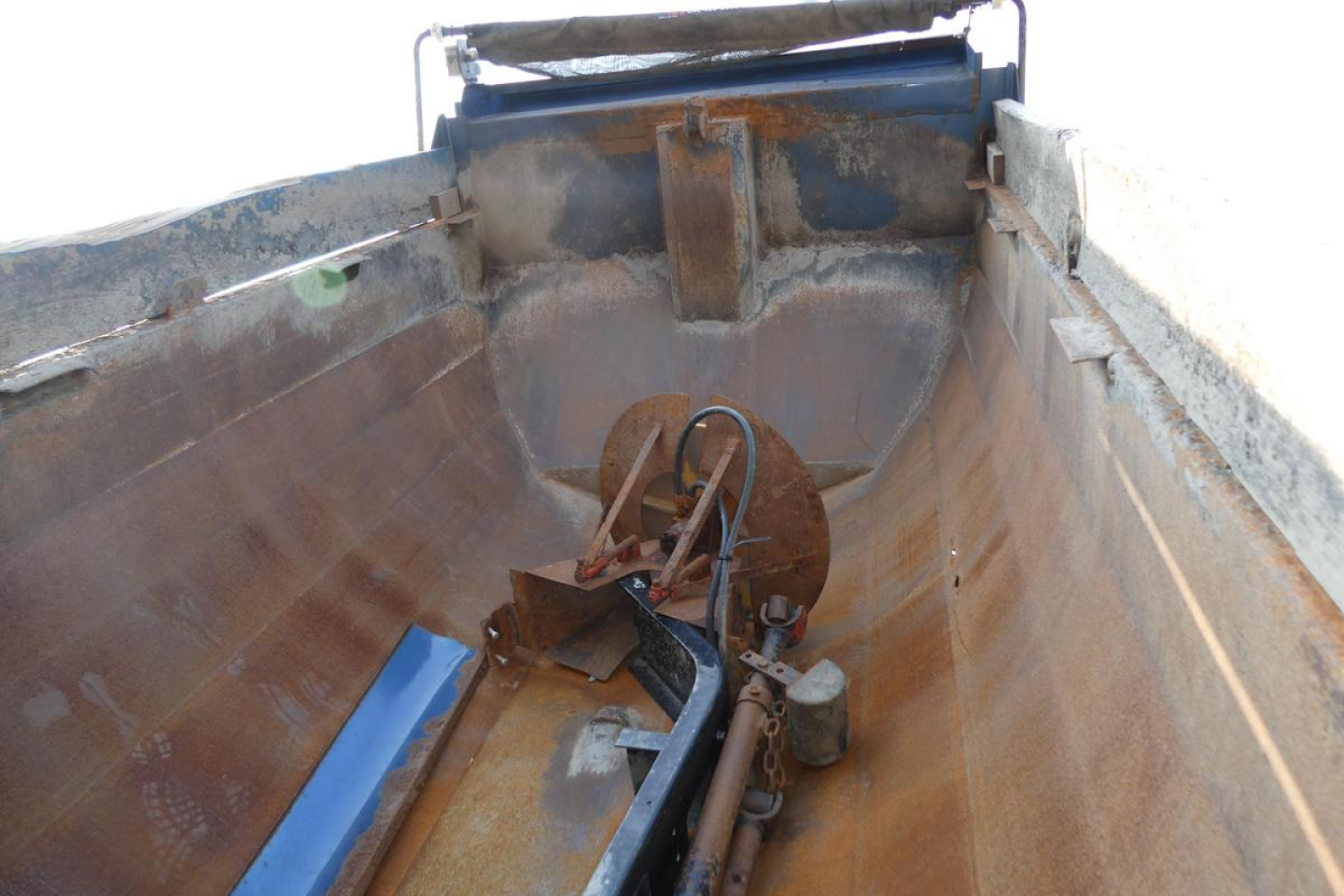 Dump truck bed interior with rusted metal walls, hydraulic or electrical components, and a circular mechanism at the front of the bed.