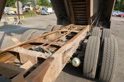 Chassis and dual rear wheels of a 2008 Mack GU713 dump truck showing a rusty frame and hydraulic components under the bed.