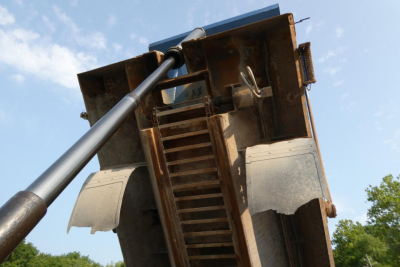 View of a Mack GU713 dump truck hopper with hydraulic piston and metal steps/ladder visible.