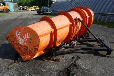 Orange snowplow or cylindrical drum attachment on trailer chassis with chains and support frame, used vehicle in yard.