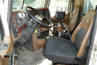 Cab interior of a Mack GU713 dump truck showing steering wheel, dashboard, and two seats with brown and black upholstery.