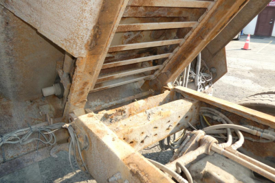 Mack GU713 dump truck chassis showing rust on frame, hydraulic lines, and underside components with exposed metal ladder and tarped area.