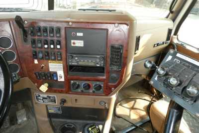Dashboard of a Mack GU713 truck showing numerous switches, climate controls, CD/radio, and beige interior with wood grain paneling.