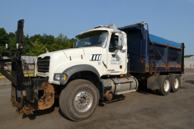 Mack GU713 dump truck in service condition showing front grille, cab, and blue dump bed with chains, side text visible