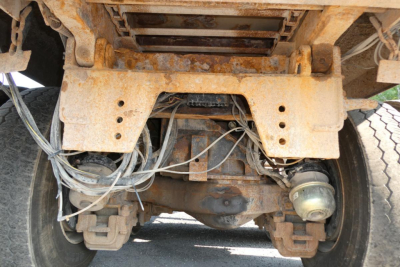 Truck rear undercarriage view showing suspension, axles, and drivetrain components with rust residue and wiring harnesses visible.
