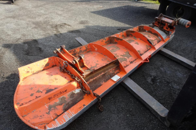 Heavy orange snow plow blade attachment with cutting edges and chains resting on pallet forks.