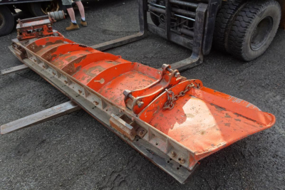Orange snow plow blade attachment on a truck chassis showing wear and hydraulic linkage