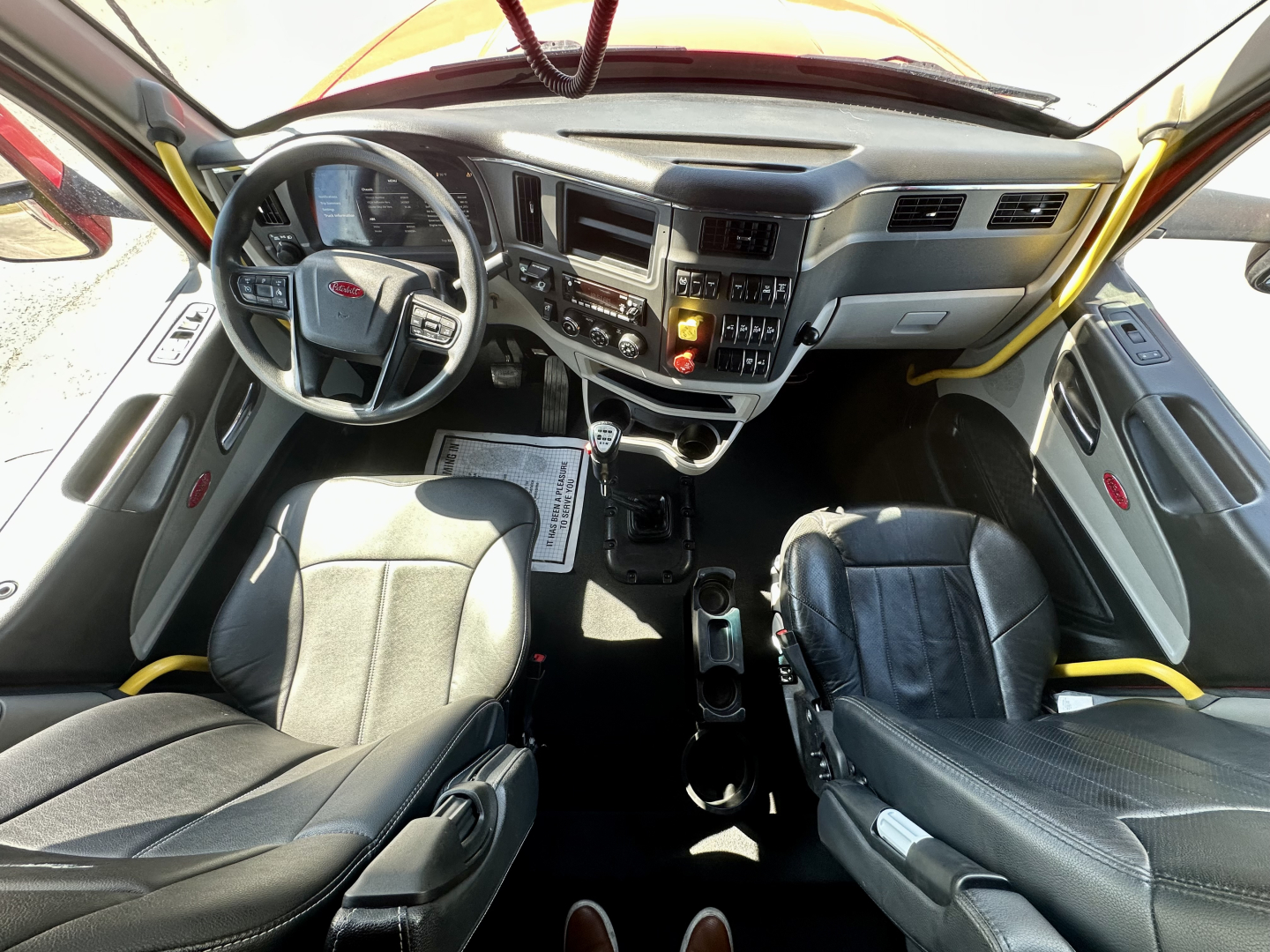 Peterbilt 567 cab interior view showing steering wheel, instrument cluster, center console, and two seats.