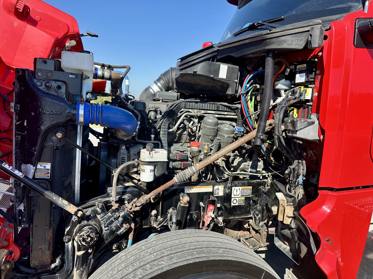 Peterbilt 567 engine bay showing various components including coolant reservoir, hoses, wiring harness, and intake with red exterior around.