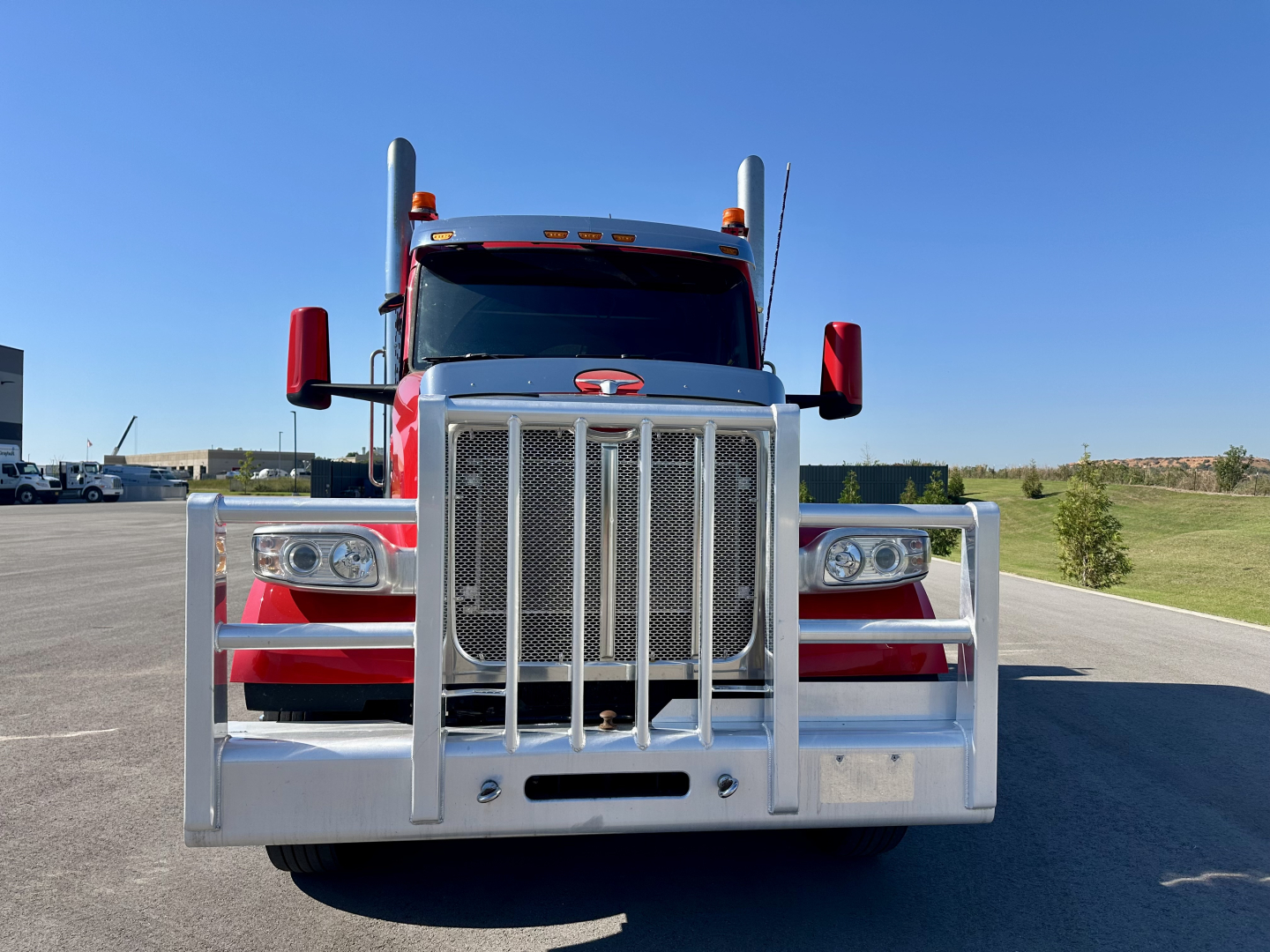 Peterbilt 567 front view showing chrome grille guard and bumper, red cab, dual tall exhausts, clear headlights.