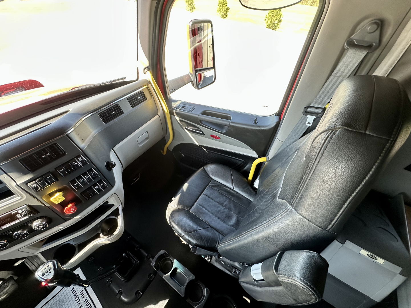 Peterbilt 567 truck cab interior view showing driver's seat and dashboard with gear shifter, steering wheel, and window controls.