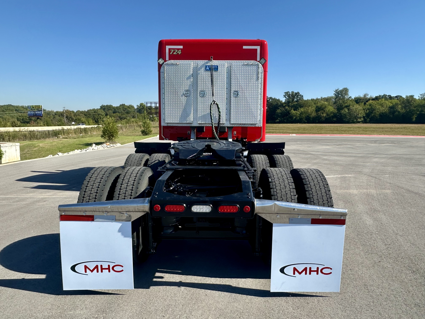 Peterbilt 567 conventional sleeper truck rear view showing dual rear axles, fifth wheel, and chrome mud flaps with MHC logos.