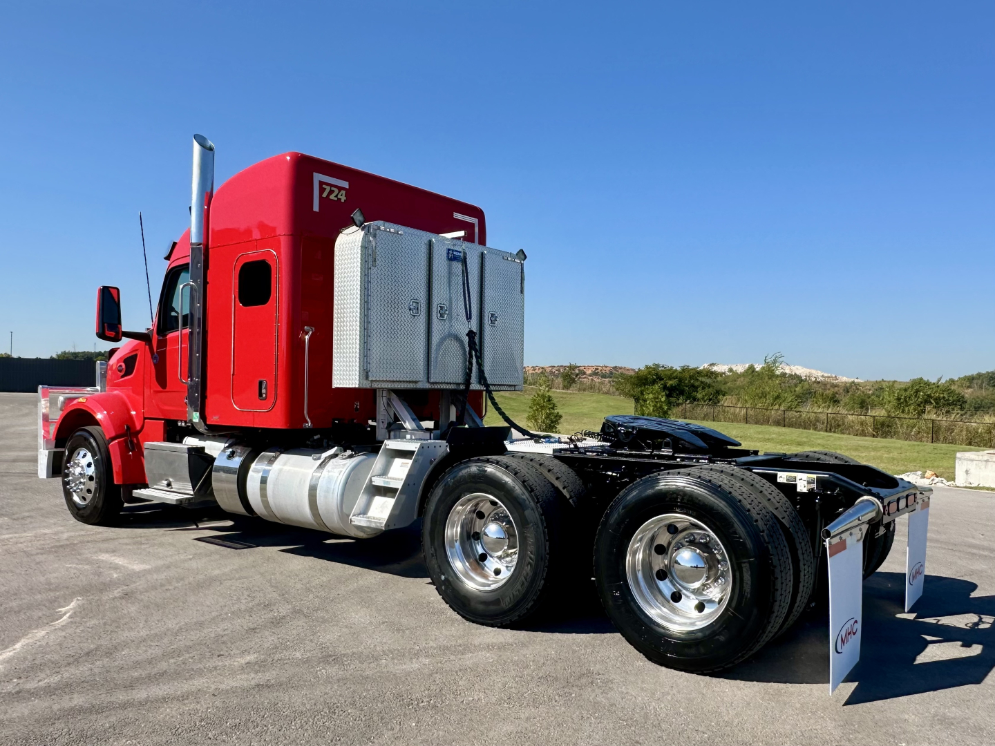 Peterbilt 567 sleeper tractor in red, side view showing fuel tanks and dual rear axles.
