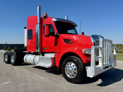 Peterbilt 567 conventional sleeper tractor in red with chrome grille, fuel tanks, dual rear axles, and front bumper guard, side view.