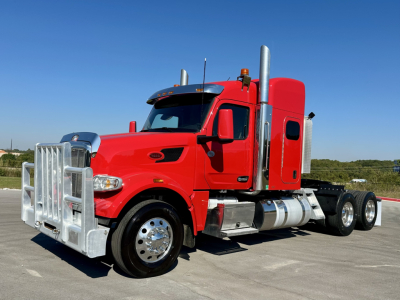 Peterbilt 567 truck in red cab with chrome bumper guard and exhaust stacks, side view showing sleeper and dual rear axles.