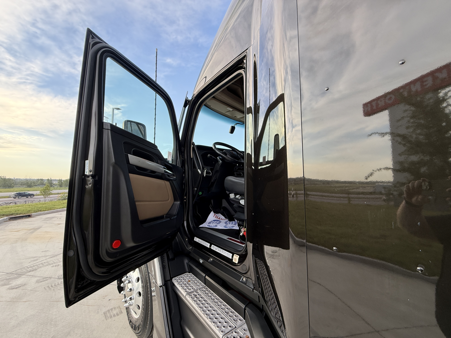 Kenworth T680 truck cab door open showing interior and steps, reflective black exterior.