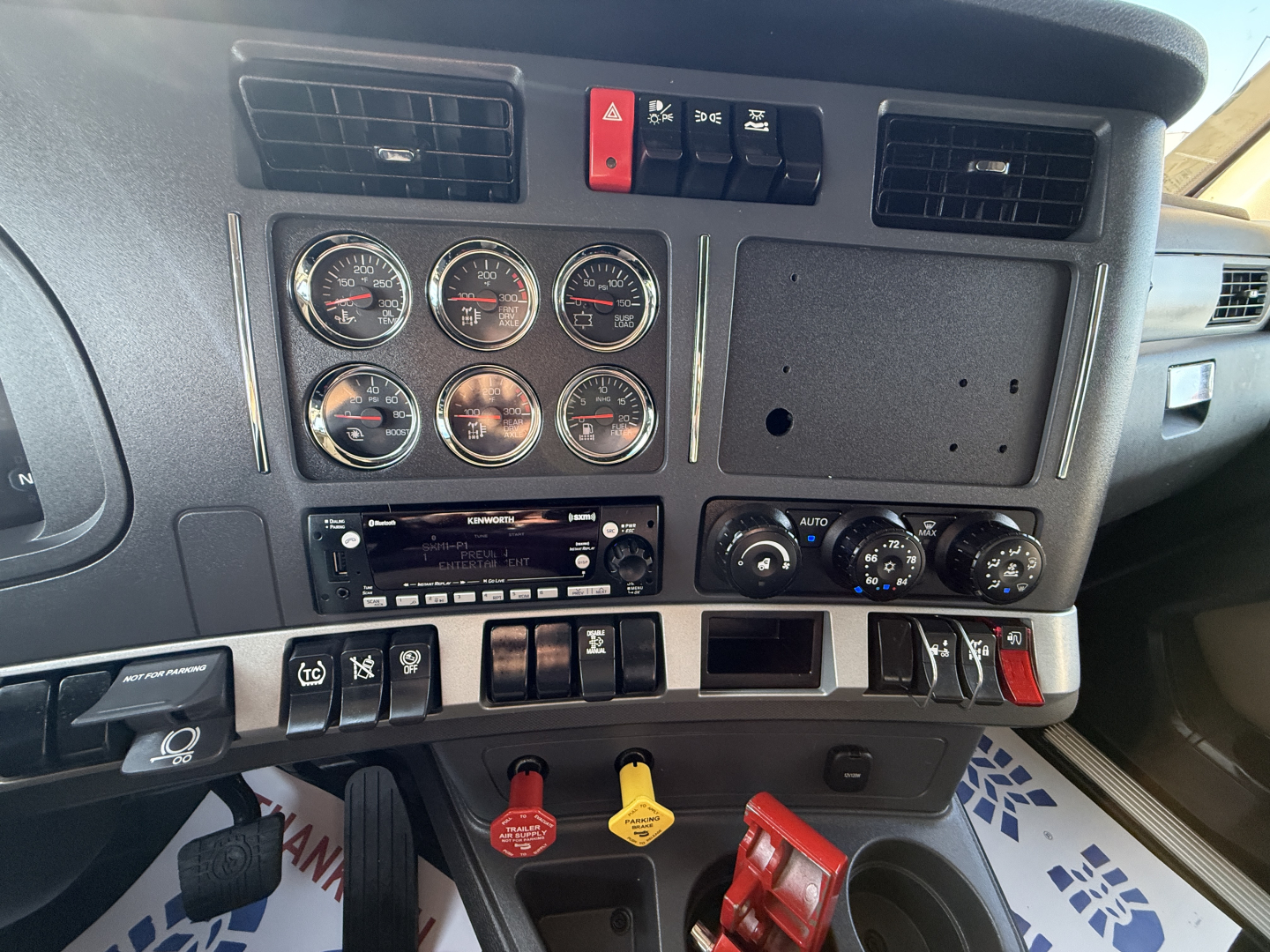 Dashboard of a Kenworth T680 with multiple gauges and switches, center area shows blank panel and climate controls, yellow and red keys nearby.