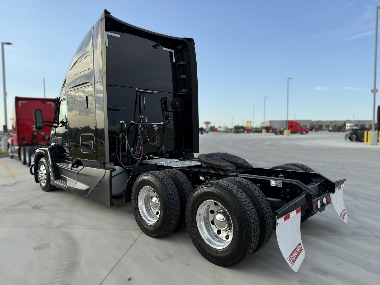 Kenworth T680 tractor rear view showing chassis and dual rear axles, black sleeper cab, chrome wheels, and white mud flaps.