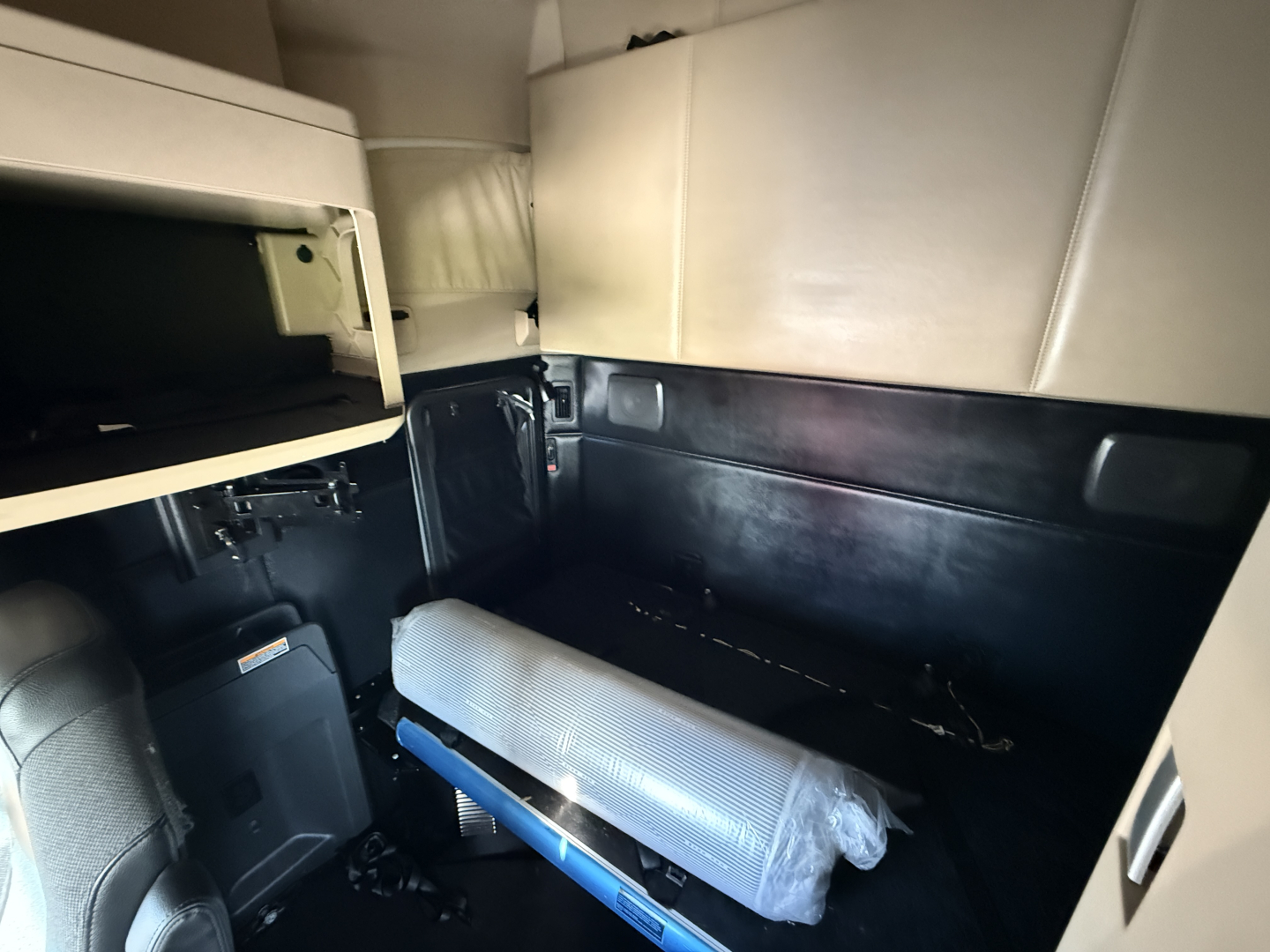 Cab interior of a 2023 Kenworth T680 sleeper truck showing seating area and storage with light gray upholstery and black panels.