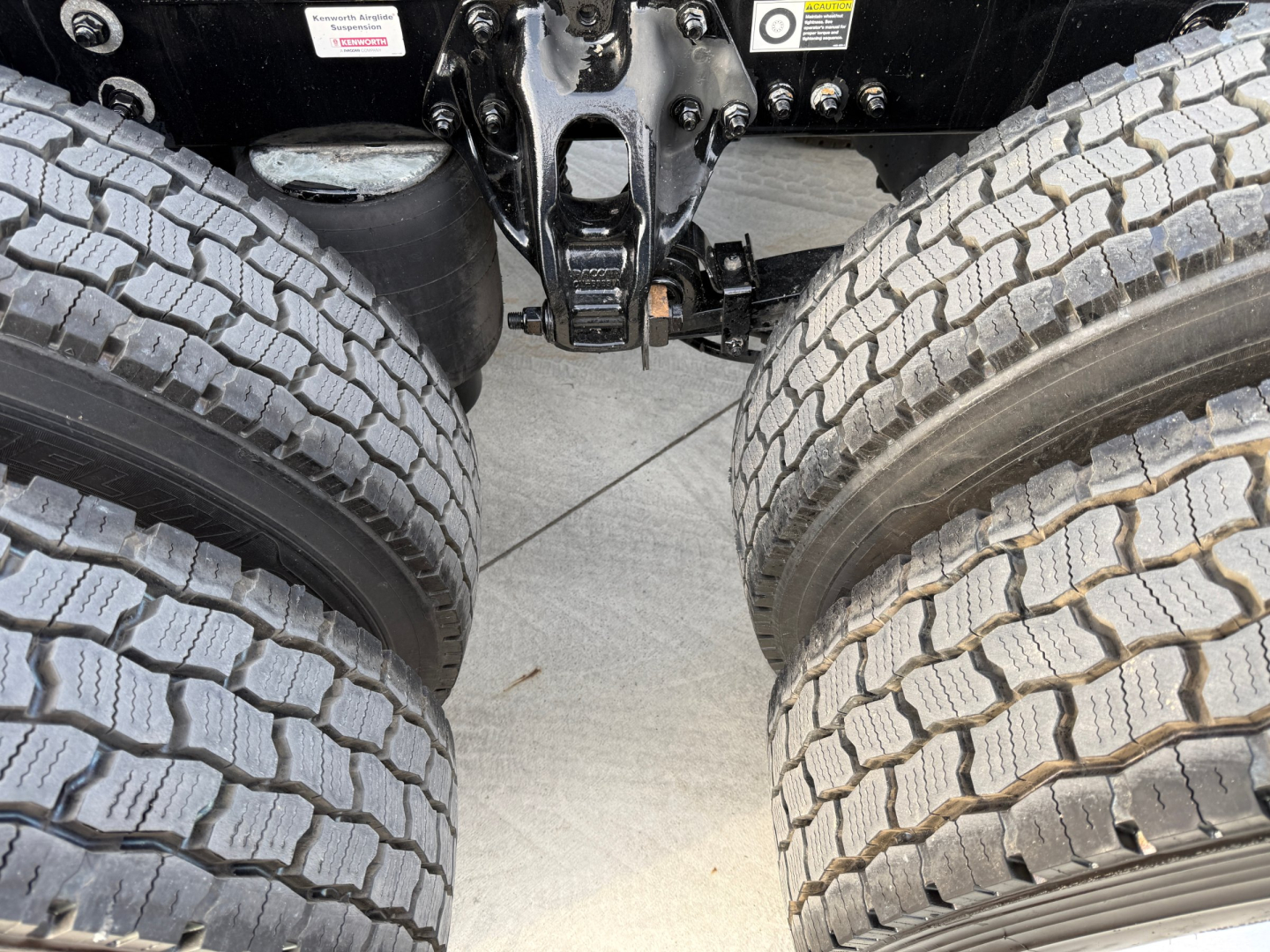 Kenworth T680 truck rearview showing dual rear axles and suspension components, tires, and undercarriage center with hitch assemblies.