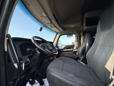 Cab interior of a 2023 Kenworth T680 truck showing steering wheel, dashboard, and driver seat with fabric upholstery and overhead compartments.