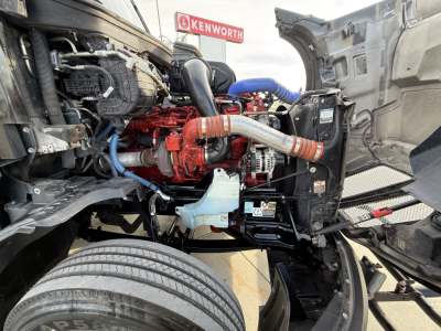 Kenworth T680 engine bay with exposed red engine and coolant hoses, visible alternator, radiator, and surrounding compartment.