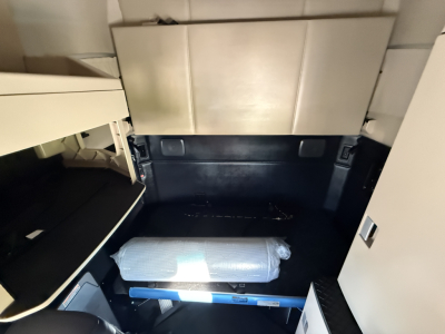 Kenworth T680 dash area with sleeper interior showing storage bed and side cabinet, interior paneling, and a packaged mattress placed on blue support rail.