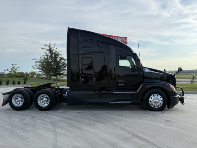 Kenworth T680 tractor-trailer side profile showing black sleeper cab and rear axles in daylight.
