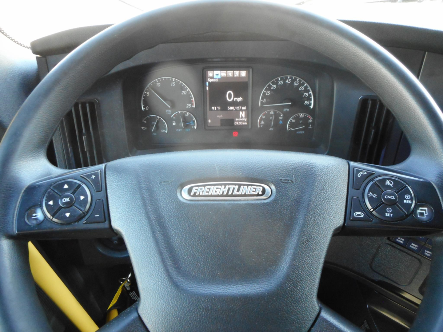Steering wheel with Freightliner logo in center and dashboard gauges visible, including digital display in center showing 0 mph and various indicators.