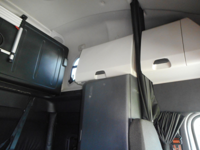 Vehicle cab interior showing storage compartments, overhead bunk area, and partition between sleeper and driving area.